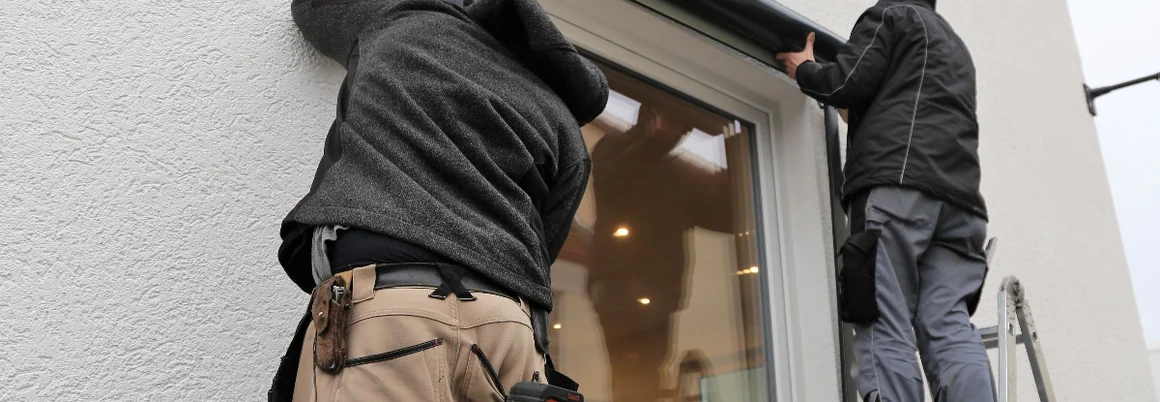 Zwei Personen montieren einen Rollladen an einem Fenster.